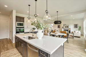 Kitchen featuring dark brown cabinetry, stainless steel appliances, a kitchen island with sink, sink, and hanging light fixtures