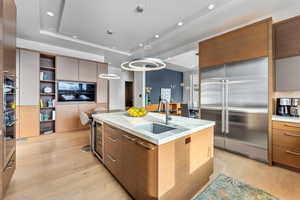 Kitchen with pendant lighting, a center island with sink, sink, a tray ceiling, and stainless steel built in refrigerator