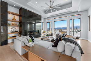 Living room featuring built in shelves, ceiling fan, a high end fireplace, light hardwood / wood-style floors, and a tray ceiling