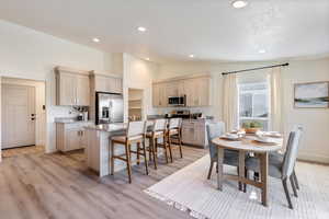 Kitchen featuring vaulted ceiling, light wood-type flooring, a kitchen island, a kitchen bar, and stainless steel appliances