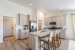 Kitchen with lofted ceiling, sink, an island with sink, appliances with stainless steel finishes, and light stone counters