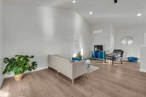 Living area featuring a wall unit AC, light wood-type flooring, vaulted ceiling, and recessed lighting