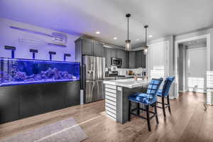 Kitchen featuring a kitchen bar, gray cabinetry, stainless steel appliances, a kitchen island with sink, and hanging light fixtures