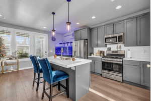 Kitchen featuring appliances with stainless steel finishes, decorative light fixtures, a kitchen island with sink, and gray cabinetry