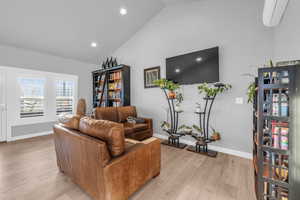 Living room featuring a wall mounted AC, high vaulted ceiling, and light wood-type flooring