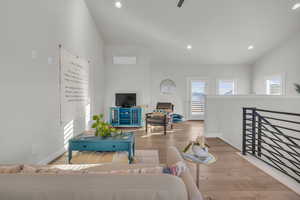 Living room with baseboards, lofted ceiling, wood finished floors, a wall mounted air conditioner, and recessed lighting