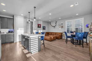 Kitchen featuring gray cabinets, a kitchen island with sink, dishwasher, and decorative light fixtures