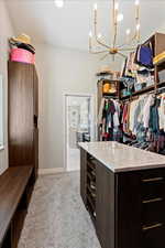 Walk in closet with a notable chandelier and light carpet