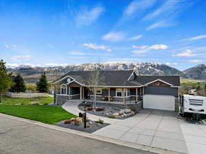 View of front of home with a mountain view, a porch, a garage, and a front lawn