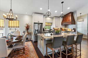 Kitchen with white cabinetry, dark hardwood / wood-style flooring, backsplash, stainless steel fridge, and custom range hood