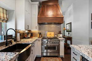 Kitchen with premium range hood, sink, white cabinets, and high end stainless steel range oven