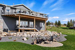 Rear view of property featuring central air condition unit, a wooden deck, an outdoor fire pit, a patio, and a lawn