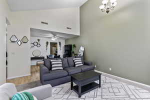 Living room featuring high vaulted ceiling, light hardwood / wood-style floors, and ceiling fan with notable chandelier