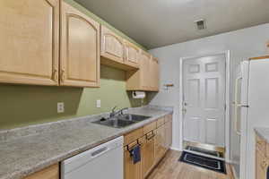 Kitchen featuring light brown cabinetry, white appliances, a textured ceiling, sink, and light hardwood / wood-style flooring