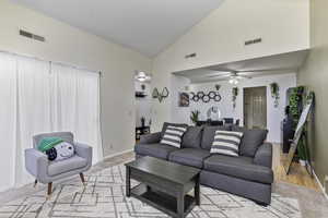 Living room with ceiling fan, light colored carpet, and high vaulted ceiling