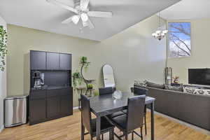 Dining room with vaulted ceiling, light hardwood / wood-style floors, and ceiling fan with notable chandelier