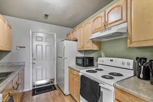 Kitchen featuring a textured ceiling, light brown cabinetry, light hardwood / wood-style floors, and white appliances