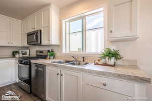 Kitchen with sink, white cabinets, dark wood-type flooring, and appliances with stainless steel finishes