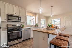 Kitchen featuring butcher block counters, white cabinetry, a center island, and appliances with stainless steel finishes