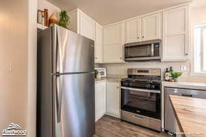 Kitchen featuring white cabinets, appliances with stainless steel finishes, butcher block countertops, and dark wood-type flooring