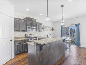 Kitchen featuring pendant lighting, a breakfast bar, a kitchen island with sink, and appliances with stainless steel finishes