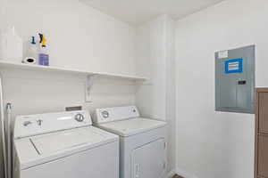 Clothes washing area featuring electric panel and washer and dryer