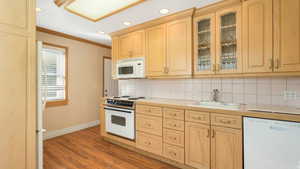 Kitchen featuring light brown cabinetry, backsplash, white appliances, sink, and light hardwood / wood-style floors