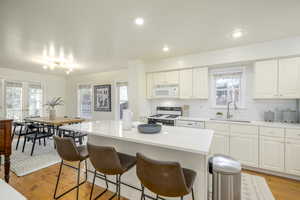 Kitchen with white cabinets, white appliances, a center island, and sink