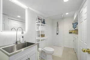 New basement bathroom featuring toilet, a tile shower, vanity, and heated tile patterned floors