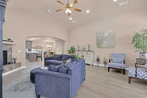 Living room with a fireplace, ceiling fan with notable chandelier, light hardwood / wood-style floors, and high vaulted ceiling