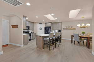 Kitchen featuring a skylight, a kitchen island with sink, black appliances, an inviting chandelier, and hanging light fixtures