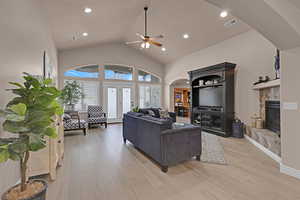 Living room featuring light hardwood / wood-style floors, high vaulted ceiling, ceiling fan, and a tiled fireplace