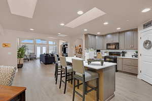 Kitchen featuring black appliances, a breakfast bar, light hardwood / wood-style floors, and a center island with sink