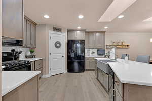 Kitchen with backsplash, black appliances, sink, a skylight, and light hardwood / wood-style flooring