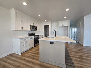 Kitchen with a kitchen island with sink, sink, hardwood / wood-style flooring, white cabinetry, and stainless steel appliances