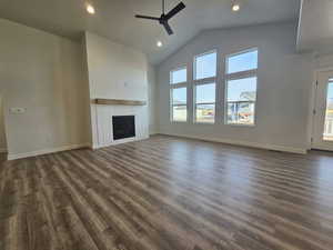 Unfurnished living room featuring dark hardwood / wood-style floors, a brick fireplace, ceiling fan, and a healthy amount of sunlight