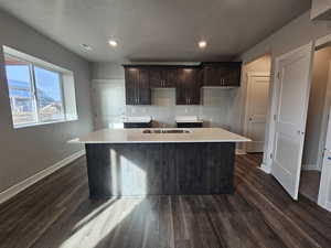 Basement Kitchen with dark brown cabinetry, an island with sink, dark wood-type flooring, and a textured ceiling