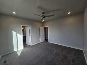 Unfurnished bedroom featuring dark colored carpet, ceiling fan, and a textured ceiling