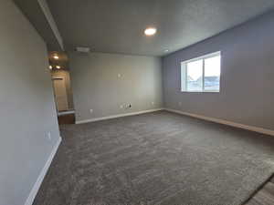 Unfurnished room featuring a textured ceiling and dark carpet