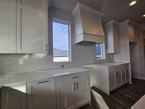 Kitchen with white cabinetry, dark hardwood / wood-style flooring, light stone countertops, and custom range hood