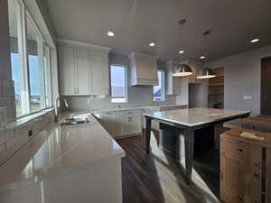 Kitchen featuring white cabinetry, sink, a center island, decorative light fixtures, and custom range hood