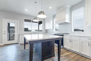 Kitchen with a breakfast bar, hanging light fixtures, stainless steel range with gas stovetop, custom range hood, and white cabinets