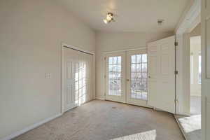 Entryway featuring vaulted ceiling, light carpet, and french doors