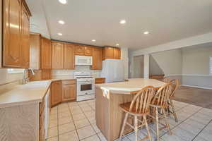 Kitchen with a kitchen breakfast bar, white appliances, sink, a center island, and light tile patterned flooring