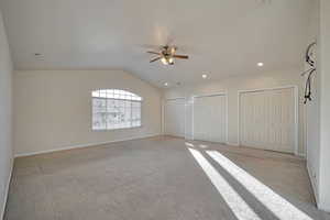 Carpeted empty room with ceiling fan and lofted ceiling