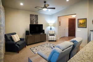 Living area featuring ceiling fan, light colored carpet, and vaulted ceiling.