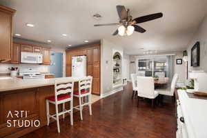 Kitchen featuring white appliances, dark hardwood / wood-style floors, ceiling fan, tasteful backsplash, and a kitchen bar