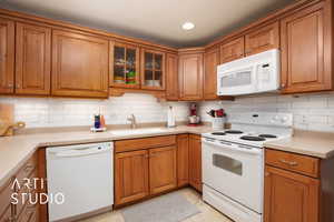 Kitchen with light tile patterned flooring, white appliances, sink, and tasteful backsplash