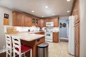 Kitchen with white appliances, backsplash, sink, light tile patterned floors, and kitchen peninsula