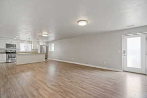 Unfurnished living room with sink, light wood-type flooring, and a textured ceiling